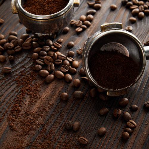 Portafilters filled with aromatic ground coffee on dark wooden surface with coffee beans